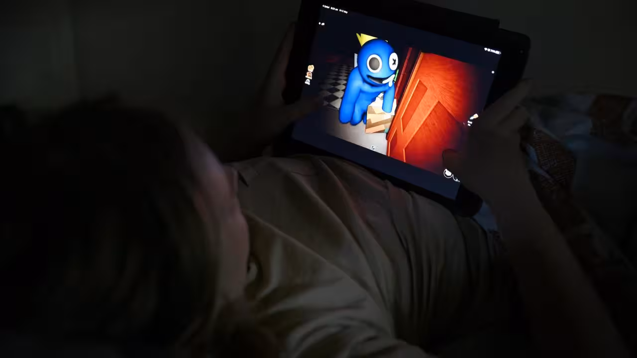 A child lying down on their back, playing a game in the dark on a tablet.